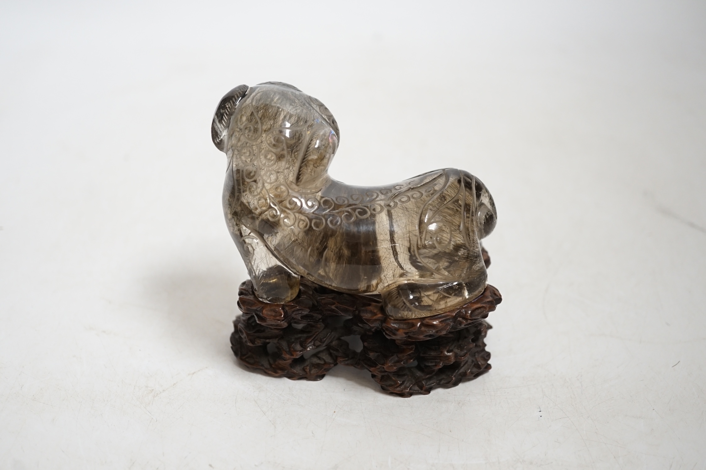 A Chinese carved smoky quartz lion dog on hardwood stand, 9.5cm wide. Condition - fair, impact damage to tail